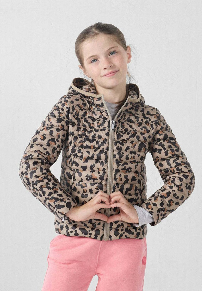 Donsjack met een luipaardprint in beige en zwart, ritssluiting en capuchon. Model draagt roze broek en vormt een hartje met de handen.