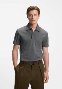 Graues Kurzarm-Poloshirt mit kragenähnlichem Ausschnitt, drei Knöpfen und strukturierter Stoff, kombiniert mit braunen Faltenhosen und einem Gürtel.