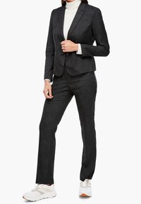 Czarny szeleszczący garnitur z dopasowaną marynarką i pasującymi spodniami, zestawiony z białymi trampkami. Gładka tekstura i zorganizowany design.