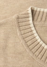 Beżowy dziany sweter z prążkowanym kołnierzem z jasnymi kremowymi akcentami. Tekstura jest miękka i gładka, podkreślając prosty, klasyczny design.