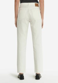 Vita denimbyxor med rak ben-design, bakfickor och en brun läderpatch på midjan. Svarta skor synliga nedanför.