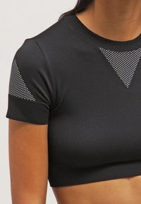 Primer plano de una persona que lleva una camiseta corta negra ajustada con detalles de malla en el pecho y las mangas superiores.