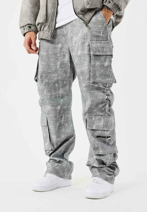Pantaloni cargo grigi con finitura testurizzata, dotati di più tasche e sottili strisce più chiare. Abbinati a sneakers bianche per un contrasto.