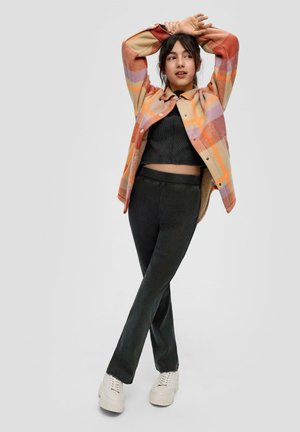 Fleece shirt in shades of orange and purple, paired with a black crop top and dark green pants. Wearing white platform sneakers.