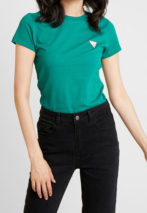 Türkisfarbenes Baumwoll-T-Shirt mit kurzen Ärmeln, rundem Ausschnitt und einem kleinen weißen Dreieck-Logo auf der linken Brust, kombiniert mit hoch taillierten schwarzen Jeans.