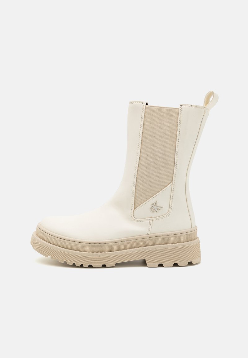 White ankle boot made of smooth leather with beige elastic side panels, chunky textured sole, and a tab for easy wear.