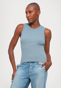 Light blue ribbed tank top with a round neckline, paired with light blue denim jeans. Smooth texture, fitted design, sleeveless style.