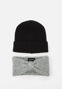 Cappello a maglia nera con texture a coste sopra una fascia per la testa grigia chiara a coste con design frontale attorcigliato e etichetta del marchio.
