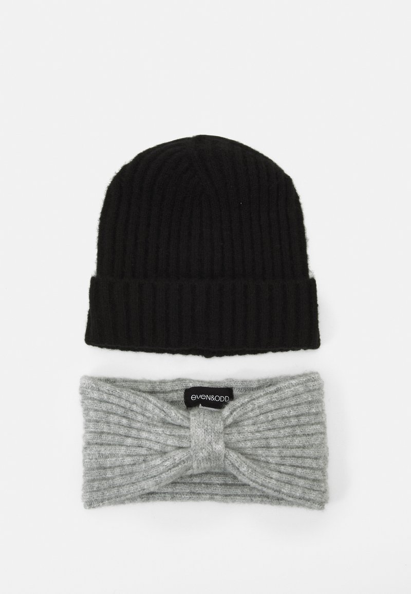 Cappello a maglia nera con texture a coste sopra una fascia per la testa grigia chiara a coste con design frontale attorcigliato e etichetta del marchio.