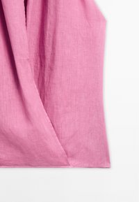 Jasnoróżowa tkanina lniana, układająca się w zwoje, ukazująca miękką fakturę. Materiał wydaje się oddychający, z subtelnym połyskiem. Widoczny złożony brzeg.