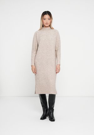 Langes, hellbeiges Strickkleid mit hohem Kragen, gerippten Bündchen und seitlichen Schlitzen, kombiniert mit kniehohen schwarzen Stiefeln. Glatte Textur.