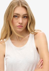 Mouwloze witte tanktop gemaakt van lichtgewicht stof, met een ronde halslijn en een subtiel merklogo op de voorkant.