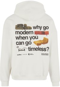 Sweatshirt blanc avec une impression graphique présentant des designs de meubles et le texte : "pourquoi aller vers le moderne quand on peut opter pour le intemporel ?" en lettres noires en gras.