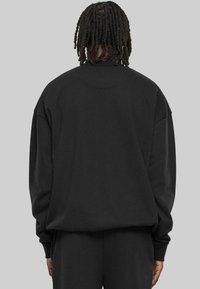 Sweatshirt noir à coupe décontractée, col rond et manches longues. Texture de tissu douce, design minimaliste sans logos visibles.
