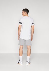 Camiseta blanca con rayas negras en las mangas, combinada con pantalones cortos grises y zapatillas blancas, vista desde la parte de atrás. Textura suave. Diseño simple.