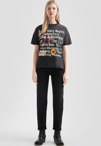 Camiseta gráfica negra con texto en blanco y colores, corte holgado, mangas cortas, combinada con pantalones negros ajustados y botas negras hasta el tobillo.