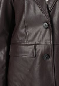 Donkerbruine leren blazer met twee zwarte knopen en een klepzak aan de linkerkant.