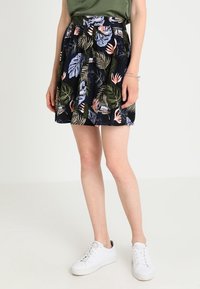 Gonna nera con motivo floreale che presenta foglie verdi e rosa, design plissettato e vita alta, abbinata a sneaker bianche.