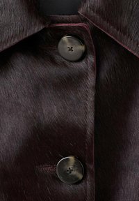 Collare in pelliccia sintetica di un intenso bordeaux scuro con due grandi bottoni rotondi. La texture è liscia con una leggera lucentezza, evidenziando l'aspetto lussuoso del capo.