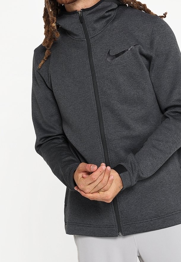 Veste zippée Nike gris foncé en tissu texturé, avec un col haut et un petit logo sur la poitrine gauche.