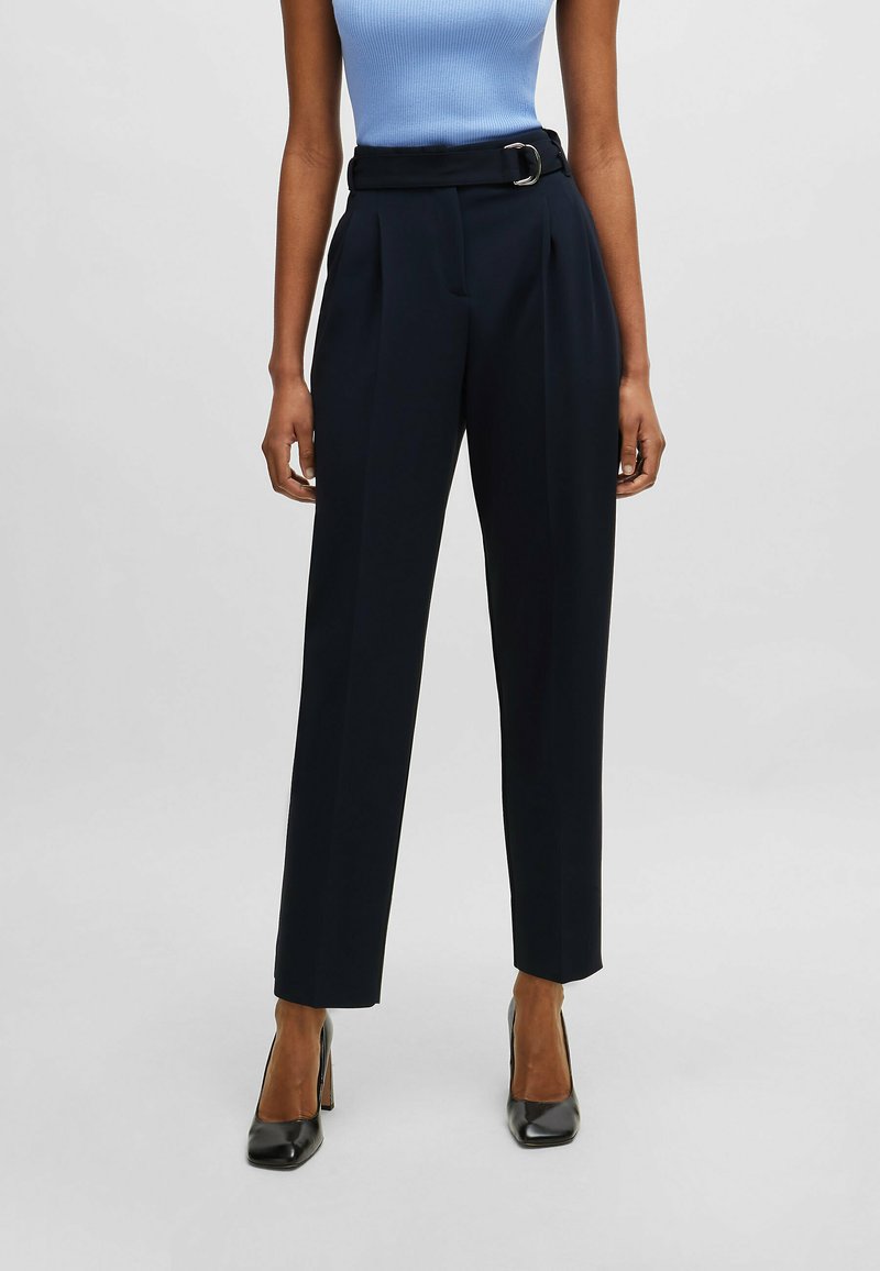 Pantaloni alta vita color navy con cintura e fibbia, caratterizzati da pieghe e una vestibilità sartoriale, realizzati in un tessuto leggero e morbido.