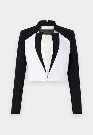 Skrajšani blazer z črnimi in belimi paneli, dolgimi rokavi in zadrgo spredaj. Ima ovratnik s poševnimi robovi in gladko teksturo blaga.