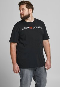 Schwarzes Baumwoll-T-Shirt mit einem weißen "JACK JONES"-Logo und einem roten Quadrat als Akzent. Kurze Ärmel, klassischer Schnitt, leichter Stretch.