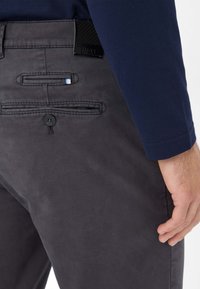 Grå bomuldsbukser med en glat tekstur, har to baglomme, en knaplukning og en lille farvet detalje i lommen.