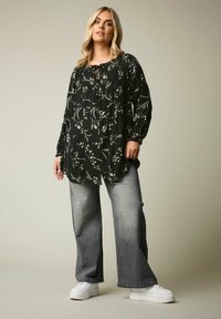 Blusa nera con fiori, maniche lunghe e scollo arricciato, abbinata a jeans grigi a gamba larga e sneakers bianchi.