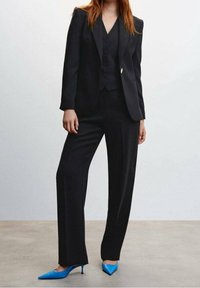 Czarny, dopasowany garnitur z marynarką o wąskim kroju, dopasowaną kamizelką i prostymi spodniami. Do tego żywe niebieskie szpilki.