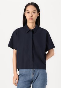 Camisa de manga corta navy con botón en el frontal, corte casual y un cuello simple. Fabricada con una tela sólida y ligera de textura suave.