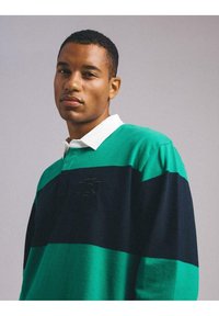 Zielono-granatowa polo z paskami, z białym kołnierzykiem, wykonana z teksturowanej tkaniny, z nadrukiem logo oraz luźnym krojem.