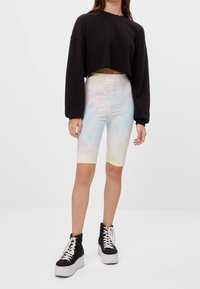 Avskuren svart sweatshirt, tie-dye cykelshorts i pastellfärger och svarta platåskor med vita snören.