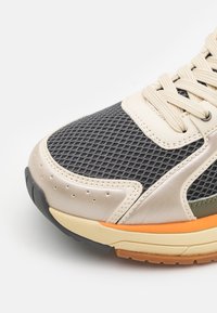 Sneaker con tomaia in mesh nera, dettagli in pelle beige e suola multicolore con particolari arancioni e verdi. Superficie testurizzata.