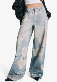 Weite Denim-Jeans mit leichter blauer Waschung, floralen Mustern und juwelartigen Akzenten in Rottönen, Grüntönen und Gold.