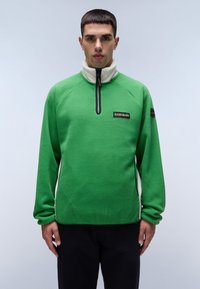 Groene fleecetrekker met een witte kraag, halfrits aan de voorkant en zwart logo-embleem. Voorzien van raglanmouwen en een textuurafwerking.