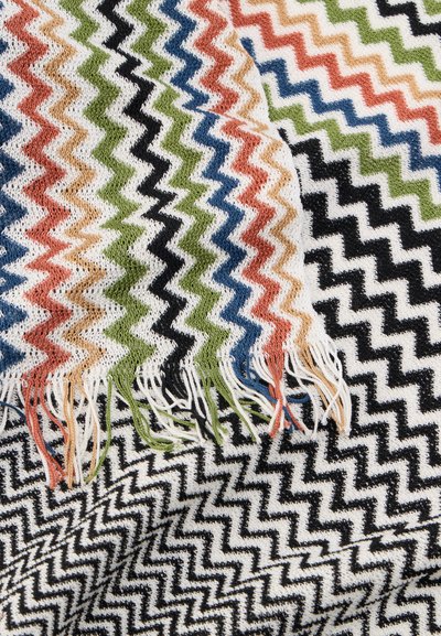 Πλεκτό ύφασμα με πολύχρωμες ζιγκ-ζαγκ ρίγες και κρόσσια στα άκρα, με νήματα σε λευκό, μαύρο, πράσινο, μπλε, πορτοκαλί και ανοιχτό καφέ.