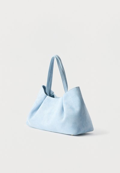 Τσάντα ώμου από σουέτ σε ανοιχτό μπλε χρώμα με δύο μακριές λαβές, σταθερή βάση και απαλά πτυχώσεις, τοποθετημένη σε λευκό φόντο.