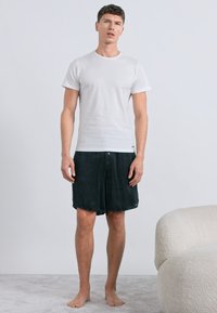 Λευκό βαμβακερό T-shirt συνδυασμένο με σκούρο πράσινο, μέχρι το γόνατο σορτς. Απλός σχεδιασμός, κοντά μανίκια, μαλακή υφή, φορεμένο χωρίς υποδήματα.