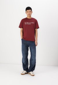 Burgundy cotton t-shirt with white text, paired with navy corduroy pants featuring distinctive patterns, and white sneakers with brown soles.
