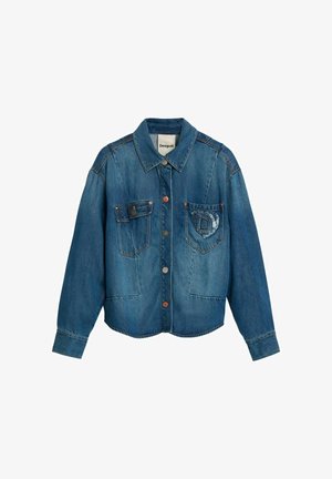 Blauwe spijkerjas met lange mouwen, knoopsluiting aan de voorkant, twee borstzakken waarvan één met een verweerde "D"-patch, en een puntige kraag.