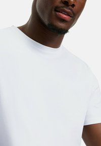 Weißes T-Shirt mit kurzen Ärmeln aus einem weichen Baumwollstoff. Runder Halsausschnitt, glatte Textur, taillierte Passform, minimale Nähedetails.