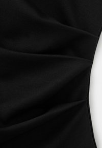 Tissu noir avec des plis diagonaux créant un motif texturé et plié sur fond blanc.