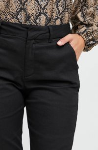 Juodos aukštos juosmens kelnės su priekinėmis kišenėmis, pagamintos iš lygaus audinio. Turi struktūrizuotą fasoną ir subtilų blizgesį. Tvirtai priglundančios prie juosmens.