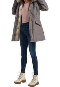 Grå parka-jakke med en hætte af kunstpels, lynlås foran og lommer. Sammen med blå jeans og hvide snøresko med en tyk sål.