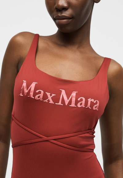 Κοντινό πλάνο ενός ατόμου που φοράει κόκκινο αμάνικο τοπ με ροζ κεντημένο κείμενο "Max Mara" και σταυρωτές υφασμάτινες τιράντες κάτω από το στήθος.