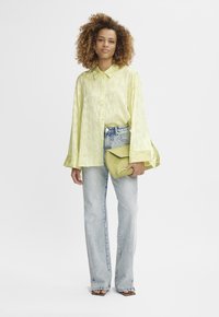 Camicia a maniche lunghe di un giallo chiaro con un motivo sottile, abbinata a jeans in denim chiaro a vita alta e una borsa a tracolla verde.