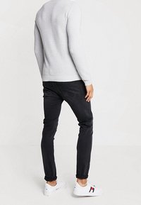 Hellgrauer, gerippter Pullover mit langen Ärmeln, kombiniert mit dunklen, eng anliegenden Jeans und weißen Sneakern mit roten und marineblauen Akzenten.