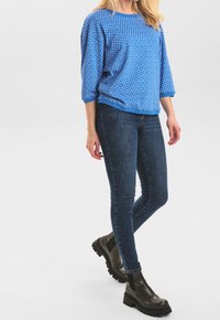 Blå mönstrad oversized sweatshirt med trekvartslång ärm, kombinerad med mörka skinny jeans och kraftiga svarta ankelboots.