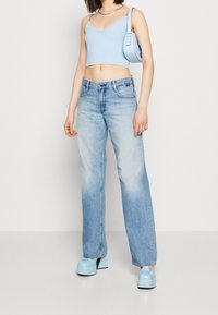 Ljusblå kort topp med spetsdetaljer, blekta blå vida jeans och blå klumpiga plattformsskor. Modellen står med avslappnade händer vid sidorna.